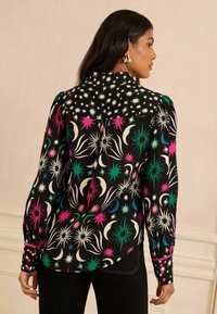 Svart skjorta med färgglada stjärn- och mån-mönster i rosa, grönt, blått och vitt, med långa ärmar och en avslappnad passform.