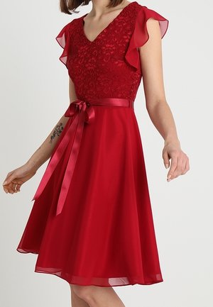 Robe rouge longueur genou avec corsage en dentelle, manches papillon, décolleté en V et ruban de satin à la taille noué en un nœud devant.