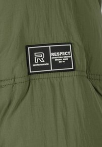 Green lightweight fabric with a crinkled texture. Features a rectangular black label with white text indicating "RESPECT" and "PERFORMANCE."