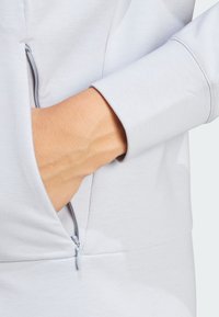 Vaaleanharmaa vetoketjullinen tasku sileällä kankaalla, jossa on resori. Resorissa on siisti sauma ja pehmeä texture, mikä korostaa käyttöä.