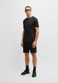 Svart träningströja och shorts-set, slät väv, korta ärmar, subtil logotyp, matchat med svarta träningsskor och solglasögon.