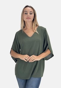 Olijfgroene, lichtgewicht top met een V-hals, korte mouwen en een relaxte pasvorm. Heeft een subtiele textuurstof en kan goed gecombineerd worden met denim.