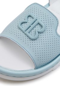 Světle modrý klouzavý sandal vyrobený z perforovaného syntetického materiálu, s výrazným pruhem ve tvaru motýla a bílou podrážkou.