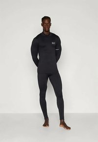 Czarny sportowy top z długim rękawem i legginsy, dopasowany krój, gładka tekstura, z małym logo na klatce piersiowej i odblaskowym akcentem.