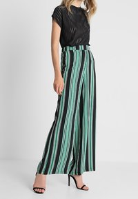 Mustat raidalliset puserot yhdistettynä korkeavyötäröisiin leveälahkeisiin housuihin, joissa on pystysuorat mustat ja mintunvihreät raidoitukset. Satiininen kangas, hienostunut tekstuuri.