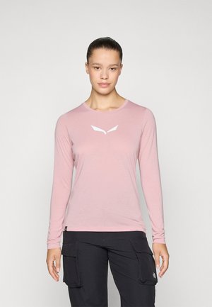 Long-sleeve, light pink shirt in soft fabric with a rounded neckline and white logo detail at the chest, paired with black cargo pants.