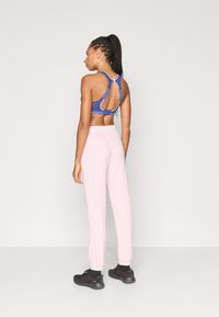 Μπλε αθλητικό σουτιέν με σχεδιασμό racerback και λεπτομέρεια με άνοιγμα, συνδυασμένο με ροζ ανοιχτό χρώμα παντελόνια jogger και μαύρα αθλητικά παπούτσια.