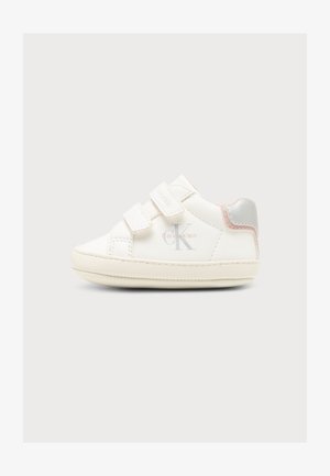 Biały dziecięcy sneaker z podwójnymi paskami na rzep, logo Calvin Klein z boku oraz srebrne i różowe detale na pięcie na jednolitym tle.