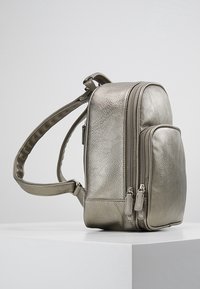 Metaliczny srebrny plecak o fakturowanej powierzchni, wyposażony w dwie zamykane na suwak przegrody i regulowany pasek. Kompaktowy i uporządkowany design.
