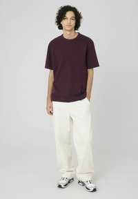 T-shirt bordeaux à manches courtes, coupe décontractée, associé à un pantalon large beige clair, porté avec des baskets de sport grises et noires.