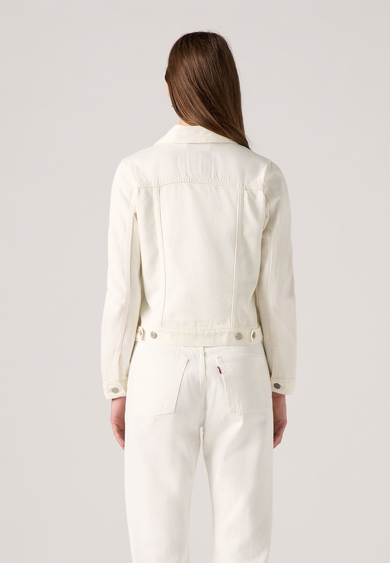 Chaqueta de mezclilla blanca con un diseño ajustado, cierres de botón y un respaldo ligeramente recortado. Estilo minimalista sin patrones ni acentos visibles.