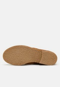 Suela de zapato de ante marrón con goma texturizada, forma redondeada y un logo estampado. Destaca por su duradera patrón de tracción y diseño acolchado.