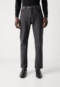 Jeans en denim gris foncé avec une coupe droite et un design à cinq poches. Dotés d'une fermeture à bouton et à glissière, ils se portent au-dessus de bottines noires.