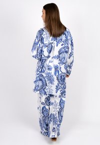 White fabric outfit featuring blue floral patterns; loose-fitting top with a tie-back detail and matching wide-leg pants.
