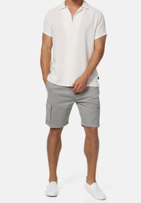 Kurzärmeliges, strukturiertes weißes Hemd mit Knöpfen, kombiniert mit hellgrauen Cargoshorts mit Seitentaschen und lockerem Sitz. Weiße Slip-on-Schuhe.