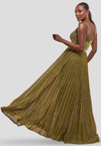 Lang, plisseret aftenkjole i metallisk olivengrøn stof, med tynde stropper og en tætsiddende bærestykke, der flyder ud i en lagdelt nederdel.