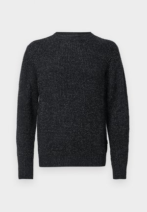 Sort og grå plettet strikket sweater med lange ærmer og ribbede manchetter, kant og rund halsudskæring vist på en hvid baggrund.