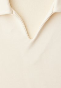 Gros plan sur une chemise beige clair à col avec une encoche en V au niveau de l'encolure et un tissu texturé à l'intérieur du col.