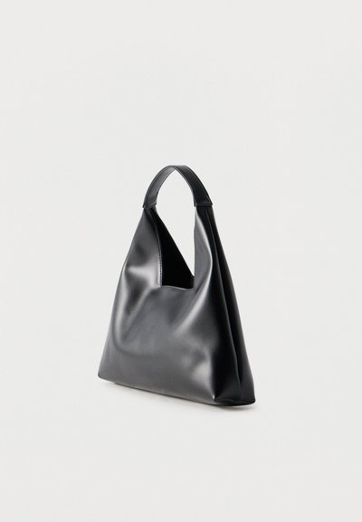 Μαύρη τσάντα από μαλακό δέρμα με μία φαρδιά λαβή και ένα τρίγωνο άνοιγμα κοντά στο πάνω μέρος, στέκεται σε λευκό φόντο.