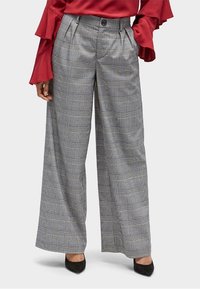 Pantalons gris à carreaux larges avec un motif à damier noir et blanc, devant plissé et taille haute, assortis à des talons noirs.
