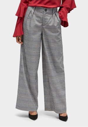 Pantalons gris à carreaux larges avec un motif à damier noir et blanc, devant plissé et taille haute, assortis à des talons noirs.