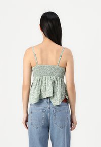Grønt blomstermønstrede peplum-top med smocket liv og tynne stropper, sammen med høyhælte lyseblå jeans.