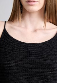 Czarny, dziany top na ramiączkach z cienkimi paskami, z wyraźnym wzorem i okrągłym dekoltem. Krój jest dopasowany i lekki.