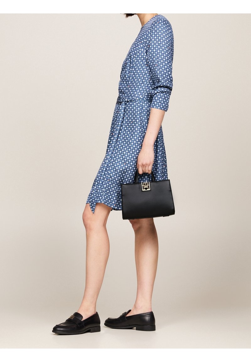 Vestido azul con lunares, de manga tres cuartos, cintura ceñida y falda acampanada, combinado con un bolso negro y mocasines negros.