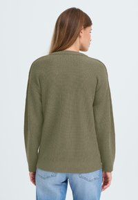 Overmatig olijfgroene trui met een textuur van gebreid patroon, geribbelde ronde halslijn en manchetten, gecombineerd met lichtblauwe jeans.