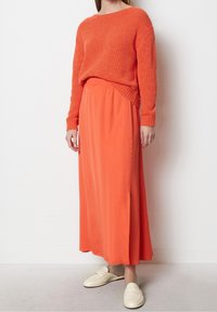Pomarańczowy sweter z dzianiny w luźnym kroju, zestawiony z lejącą pomarańczową spódnicą maxi z bocznym rozcięciem i kremowymi butami wsuwanymi.