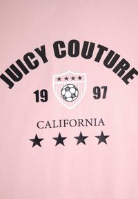 Šviesiai rožinė medvilninė marškinėliai su ryškiu juodu tekstu, skaitančiu "JUICY COUTURE", futbolo kamuolio grafika, skydas su žvaigždėmis ir "CALIFORNIA".