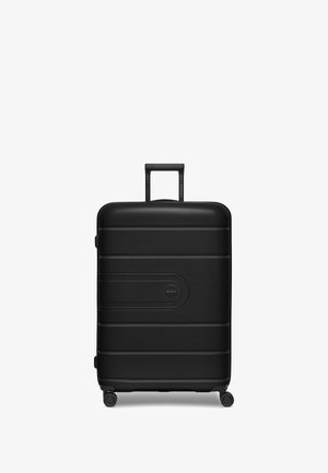 Valigia rigida nera con superficie texturizzata, scanalature orizzontali, manico telescopico e quattro ruote piroettanti per una facile manovrabilità.