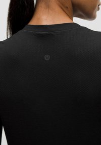 Črn športni dolg rokav vrh s teksturiranim vzorcem, okroglo ovratnikom in majhnim logotipom blagovne znamke na zgornjem hrbtu.