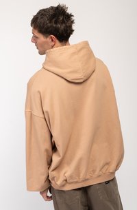 Hanorac oversized bej cu o glugă mare, umeri lăsați și tiv cu nervuri. Material moale cu o textură netedă, fără modele vizibile.