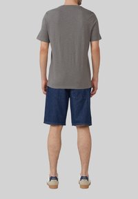 Grijze t-shirt met korte mouwen en een ronde hals, gecombineerd met blauwe spijkerbroekshorts en beige sneakers met marineblauwe accenten, gezien van achteren.