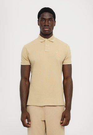 Beige polo shirt met een kraag en korte mouwen. Heeft een subtiel geborduurd logo op de linkerkant van de borst. Glad, textuurstof.