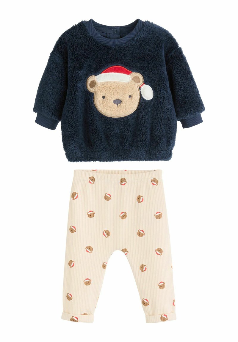Marinblå fluffig topp med björns ansikte och tomteluverdesign; beige ribbade byxor med upprepade pepparkaksdekorer och uppvikta manschetter.