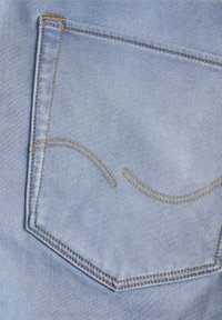 Un bolsillo trasero de mezclilla azul claro con costuras decorativas en naranja contrastante, que presenta costuras curvas y un borde superior reforzado.