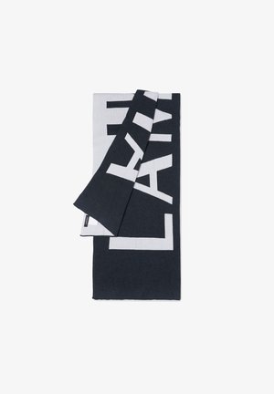 Textil alb-negru cu litere mari, îndrăznețe. Materialul pare moale, cu o textură netedă și un design stratificat.