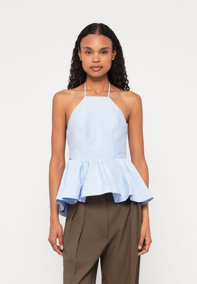 Top peplum azzurro chiaro con scollo a halter, texture morbida e bordo a volant stratificato. Abbinato a pantaloni marroni a vita alta.