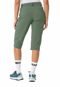 Olivgrüne Caprihosen mit einem taillierten Bund, umgeschlagenen Säumen und atmungsaktivem Stoff. Kombiniert mit blauen Wanderschuhen und weißen Socken mit schwarzen Akzenten.