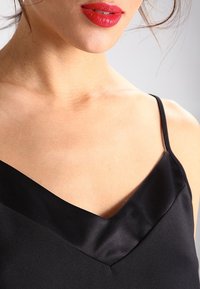 Camisole en satin noir présentant un décolleté profond en V et de fines bretelles spaghetti, avec une texture lisse et un style minimaliste.