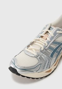 Αθλητικά παπούτσια με επάνω μέρος από διχτυωτό ύφασμα σε εκρού απόχρωση, ασημί λεπτομέρειες και μπλε ρίγες; περιλαμβάνουν μπεζ κορδόνια και υφασμάτινη μαύρη σόλα.