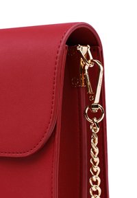Červená kožená kabelka se zlatým řetízkovým popruhem a sponou. Má hladký povrch a prošívané okraje. Design se skládacím klopou.