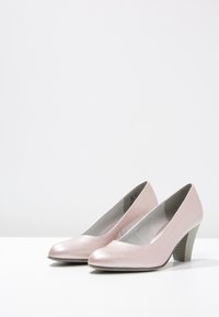 Vaaleanpunaiset korkokengät, joissa on teksturoitu pinta. Ominaisuuksiin kuuluu pyöreä kärki, tyylikäs päällinen ja keskipitkä paksu korko, jossa on uritettu muotoilu.