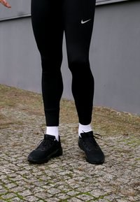 Schwarze Sportleggings mit passendem Schnitt, kombiniert mit schwarzen Sneakers mit strukturiertem Obermaterial und weißen Sportsocken.