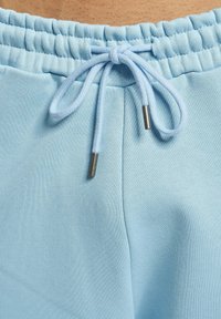 Pantaloni jogger de culoare albastră deschisă, cu un tiv reglabil, având o textur�ă moale și vârfuri metalice pe șnur. Material neted și elastic.