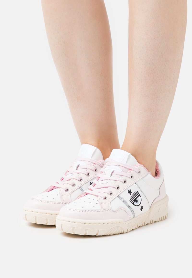 Weiße und rosa Sneaker mit strukturierten rosa Akzenten, durchlöchtem Zehenbereich, silbernem Glitzerdesign und schwarzem Aufdruck an der Seite.