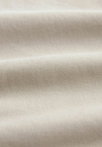 Tissu couleur crème avec une texture lisse et fine et un motif de tissage en diagonale, présentant de légères ondulations et une finition douce.