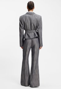 Costume gris à fines rayures avec taille ceinturée, pantalon à jambes larges, et blazer ajusté avec col à encoches et tissu texturé.